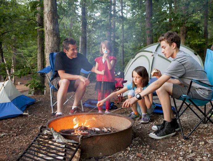 father camping with kids while kids roast marshmallows